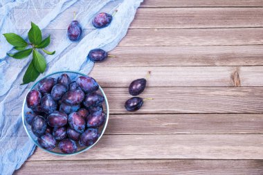 Kasede yeşil yapraklar ve tahta arka planda peçete olan erikler. Üst görünüm.