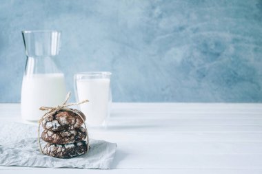 Taze pişmiş çikolatalı kurabiyelerin ve bir bardak sütün kırsal ahşap masa üzerindeki gri arka plan manzarası..