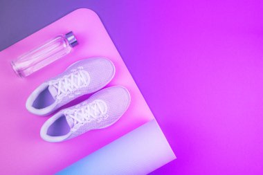 Neon mor ve pembe renkli spor ayakkabıları, yoga minderi, metin için yeri olan yeniden kullanılabilir eko cam su şişesi. Yoga, pilates ya da fitness pratiği. Kilo verme ve spor konsepti. 