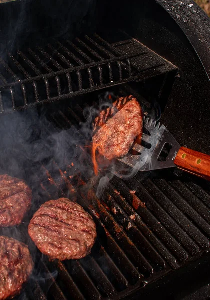 Carne asada barbacoa hamburguesa empanada para hamburguesa en utensilios de espátula metálicos que utilizan para convertir la barbacoa a la parrilla en llamas. —  Fotos de Stock