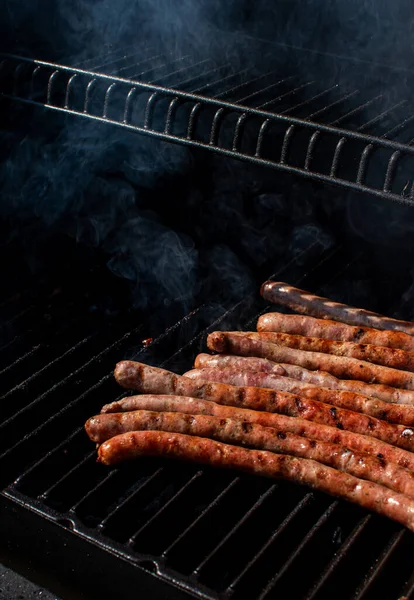 Saucisses rôties cuisant sur un barbecue au barbecue flamboyant avec de la fumée. — Photo