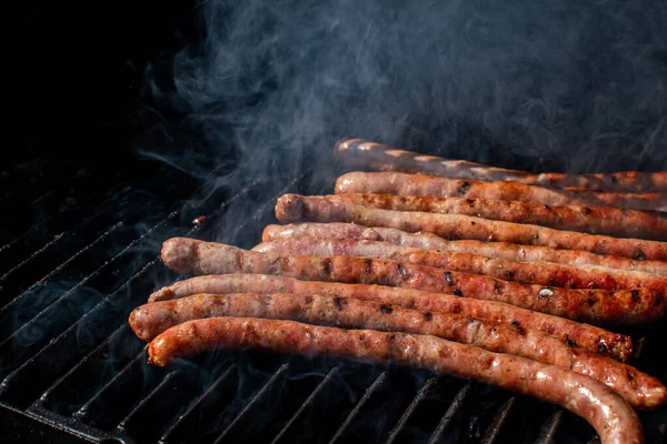 Saucisses rôties cuisant sur un barbecue au barbecue flamboyant avec de la fumée. — Photo