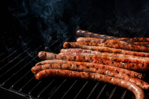 Saucisses rôties cuisant sur un barbecue au barbecue flamboyant avec de la fumée. — Photo