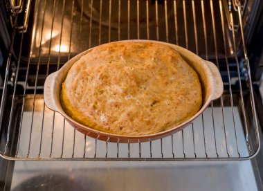 Taze somun, seramik tabağı sıcak fırına koyar. Kahverengi kabuk üst yüzeyi kaplar. Işık arka taraftan geliyor. Şeklini açıkça gösteriyor. Kapı kolları yan tarafta görünüyor. Kapı açık, tepsinin altındaki boşluğu gösterir.
