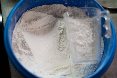 Mavi kasede un var. Şeffaf ölçüm kabı yan yatar. Ölçekli baskı unlarda görülebilir. Etrafta başka eşya yok. Sahne mutfak hazırlıklarını gösteriyor.