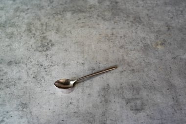 Çay kaşığı gri mutfak tezgahında duruyor. Çapraz yerleştirilmiş metal aletler. Tezgah sade bir görünüm sergiler. Nesne temiz bir tasarım gösteriyor. Yerleştirme basit kalıyor, tam olarak. Edge net, saf işaret verir, geçerlidir.