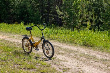 a children's bicycle with a yellow frame stands on a country village road on a bright sunny day in summer