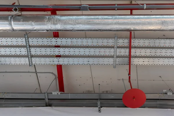 red pipe of a fire extinguishing system under the ceiling. pipe with foil insulation and trays with electric cables located in the same place