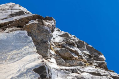 Açık gri mermerden yapılmış ve keskin kenarları olan menteşeli bir kaya, güneşli bir yaz gününde açık mavi gökyüzünün arka planına doğru fotoğraflandı..