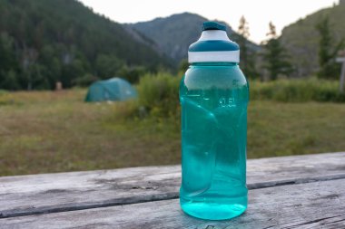 Ahşap bir masada, arka planda çadırları yakın çekim olan bir su şişesi. Yürüyüş konsepti