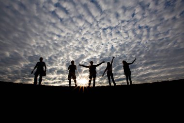 Arka tarafta muhteşem bir bulut ve el ele zıplayan siluet modeller.