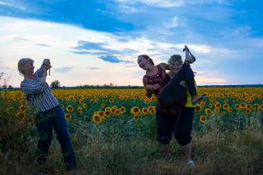 Üç orta yaşlı kadın arkadaş şakalaşıyor, eğleniyor ve ayçiçeği tarlasında gülüyorlar.