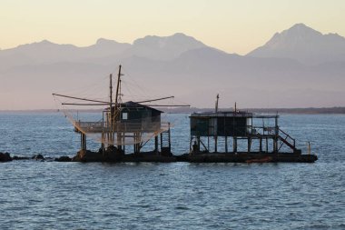 Marina di Pisa limanının kıyısında deniz ağları olan balıkçı kulübesi günbatımı gökyüzü ve dağlarının arka planına karşı