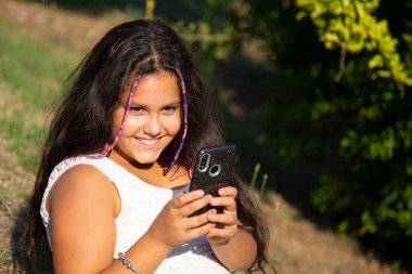 Uzun siyah saçlı çingene kız akıllı telefonuyla selfie çekiyor.