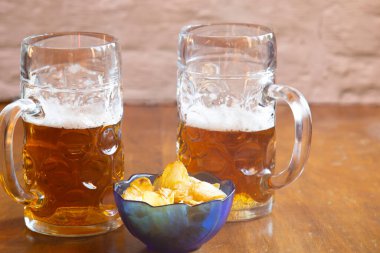 Bardaki ahşap bir masada iki büyük bardak bira ve cips.