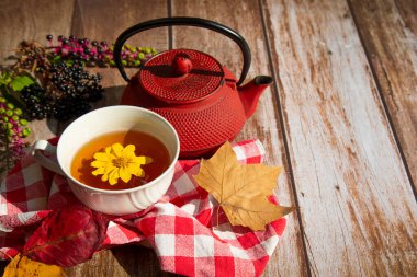 Tahta bir masada kırmızı bir çaydanlık, beyaz bir fincan çay, sarı ve kırmızı sonbahar yaprakları, siyah böğürtlen