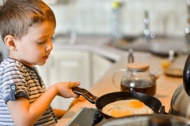 Mutfakta küçük bir çocuk kahvaltı için çırpılmış yumurta pişiriyor.