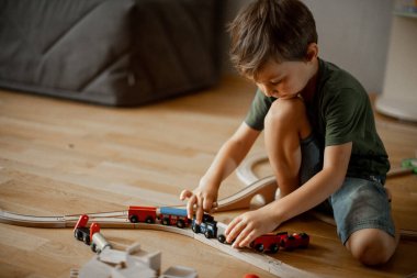 Evde, yerde, ahşap bir demiryolu ile oynayan beş yaşında bir çocuk.