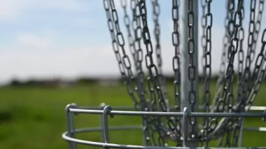 Disk golfü gol zincirleri rüzgarda yavaşça sallanıyor ve arka planda yeşil bir saha var.