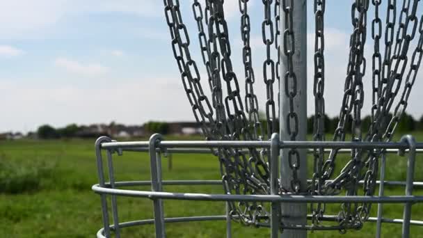 Disc golf goal kettingen zachtjes zwaaiend in de wind met een groene baan op de achtergrond — Stockvideo