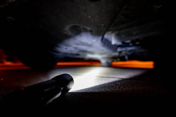 Дивлячись під позашляховиком вночі з ліхтариком, щоб перевірити проблеми — стокове фото