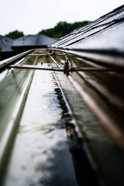 Focus selettivo su una sezione di grondaie residenziali con gancio che trasporta acqua durante una tempesta. Spruzzi e gocce di pioggia visibili. — Foto Stock