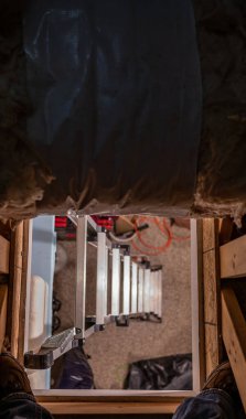 Tavan arasına açılan merdivenin altından aşağıya bakıyor.