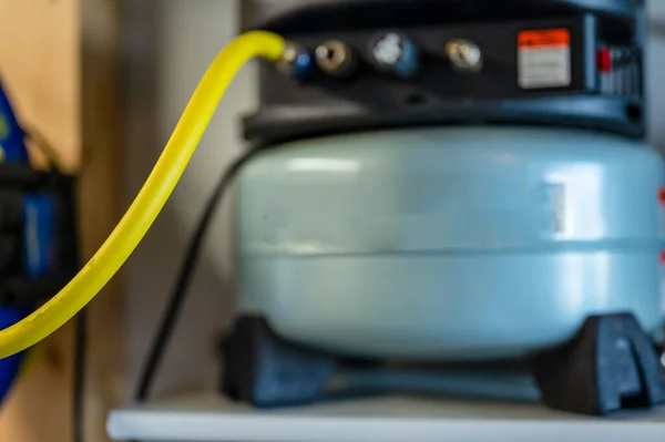 Selektiver Fokus auf einen Schlauch, der mit einem Pfannkuchen-Luftkompressor verbunden ist, der auf einem Regal sitzt — Stockfoto