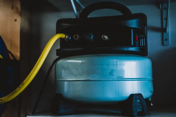 Selektiver Fokus auf einen Schlauch, der mit einem Pfannkuchen-Luftkompressor verbunden ist, der auf einem Regal sitzt — Stockfoto