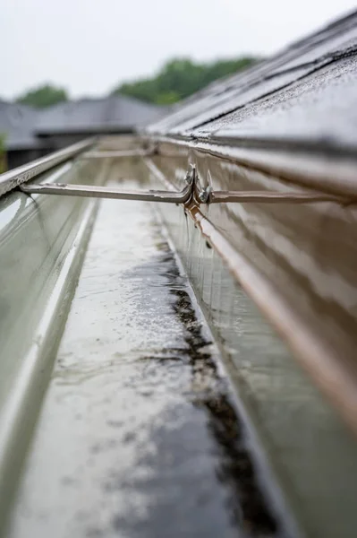 Enfoque selectivo en una sección de canaletas residenciales con suspensión que transporta agua durante una tormenta. Salpicaduras de lluvia y gotas visibles. — Foto de Stock