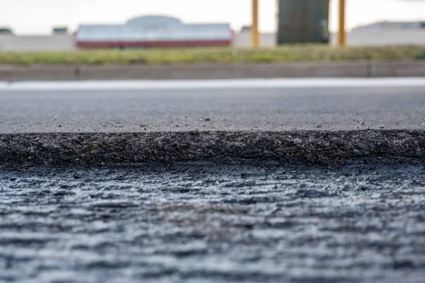 Enfoque selectivo de bajo ángulo en pavimentación de recubrimiento de asfalto en la parte superior de una base de hormigón de una calle residencial — Foto de Stock