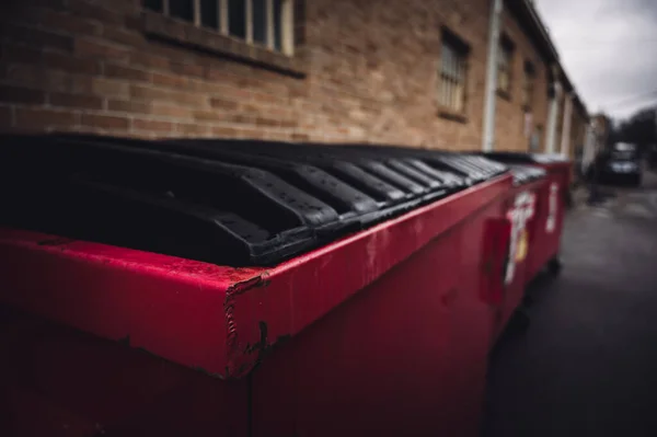 Fila de cubos de basura cubiertos a lo largo de una pared de ladrillo en un callejón trasero —  Fotos de Stock