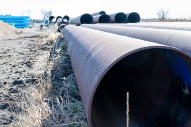 Uzun metal borular açık gökyüzünün altındaki bir inşaat sahasının zemininde düzenlenir. Dekor, etrafında çimenler büyüyen tipik bir sanayi manzarasını tasvir ediyor.