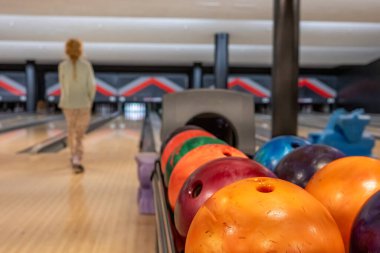 Parlak bir bowling salonunda bir kişi bowling salonuna doğru yürür. Renkli bovling topları ön planda dizilmiştir, eğlenceli bir akşam boyunca oynamaya hazırdırlar..