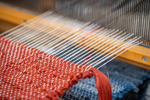 Artisans skillfully work at a loom, weaving threads into a textured fabric during the day. The warm colors and detailed patterns reflect their dedication to this craft.