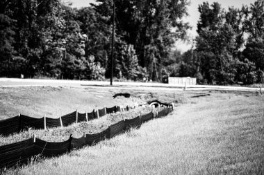 İnşaat alanında erozyonu önlemek için siyah alüvyon var. Yakınlarda yemyeşil çimenler yetişiyor, arka planda ağaçlar ve depolama konteynerleri görünüyor..