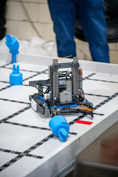 Sınıfta işaretli bir yüzey üzerinde bir robot oturuyor. Öğrenciler robotun masaya konan mavi engelleri aşmaya programlandığını izliyor..