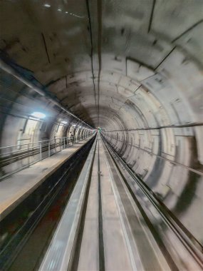 Manzara bir metro tünelini gösteriyor. Uzağa giden raylar var. Duvarlar beton ve ışıklar açık. Sahne, gece saatlerinde bir şehrin içinde..