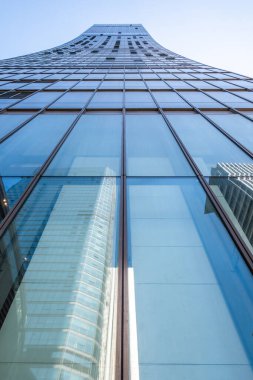 Chengdu 'da açık mavi gökyüzüne çarpıcı bir şekilde yükselen parlak bir gökdelen. Cam cephe diğer binaları yansıtıyor. Canlı bir şehir ortamında modern mimari sergileniyor..