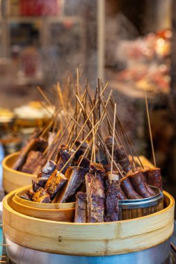 Salamura edilmiş et şişleri, Sichuan, Chengdu 'da bir sokak pazarında bambu sepetlerinde sergileniyor. Manzara canlı, ızgara yemek aroması ve aç ziyaretçilerin telaşıyla dolu..