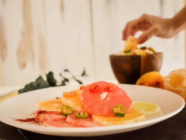 Uu mano tomando una naranja y plato de fruta refrescante con chile