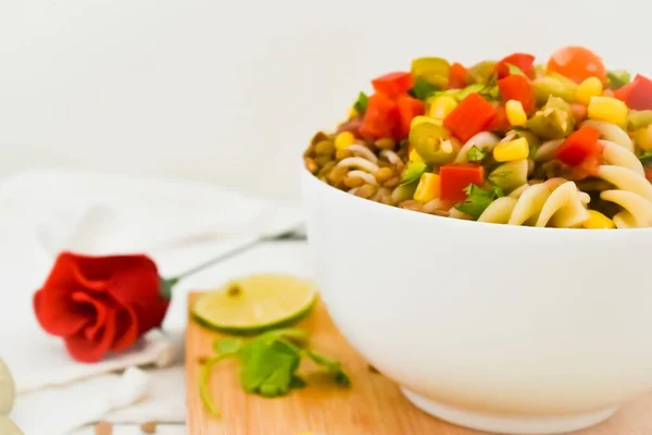 Makarnalı mercimek salatası ve sebze doğrama tahtasında kırmızı gül.