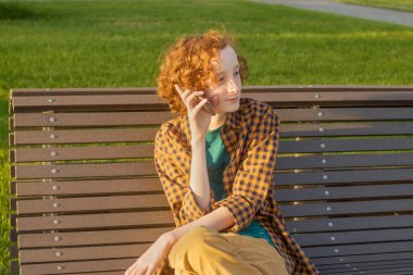 Metin için boş alan. 12-14 yaşlarındaki akıllı telefonlu bir çocuk açık hava bankında oturuyor..