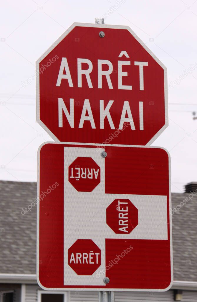 red and white stop sign with stop text in French and local native canadian Innu language (arrt means stop, nakai means stop)