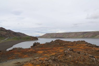 İzlanda 'daki Kleifarvatn Gölü' nün panoramik görüntüsü demir oksitten gelen kırmızı, turuncu ve koyu renkli kayalar, gri havayla çelişiyor.