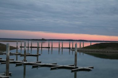 Fransa, Lac du Der 'deki marinanın huzurlu akşam manzarası, sakin su, pastel gökyüzü ve yumuşak günbatımı yansımaları ile sakin bir atmosfer yaratıyor..