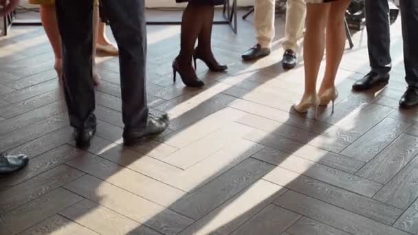 屋内イベントで靴の中の男性と女性の足 人々のグループが屋内に移動立っている 床の上の日差しと人の影 — ストック動画