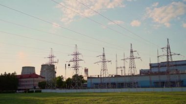 Fabrikada yüksek voltajlı elektrik hatları. Üretim, gökyüzü ve yeşil çayır. Dönüştürme istasyonu ve elektrik santrali