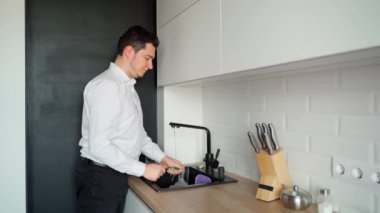 Parlak bir mutfaktaki lavaboda bulaşıkları yıkayan bir adam. Siyah lavabo. Erkek, 30 'lu yaşlarda, beyaz ırktan. Ev işi ve mutlu koca konsepti
