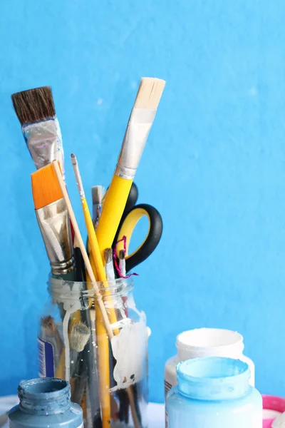 Paintbrushes in glass jar and open container of colors — Stock Photo, Image